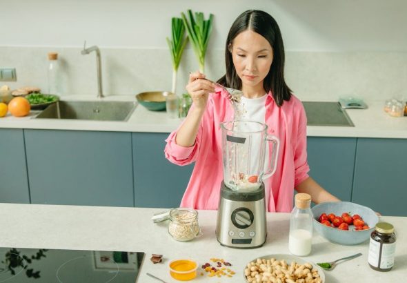 A woman in a kitchen preparing a nutritious smoothie with fresh ingredients.