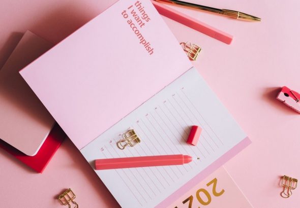 Organized workspace with pink planner, pen, and clips on pastel background.